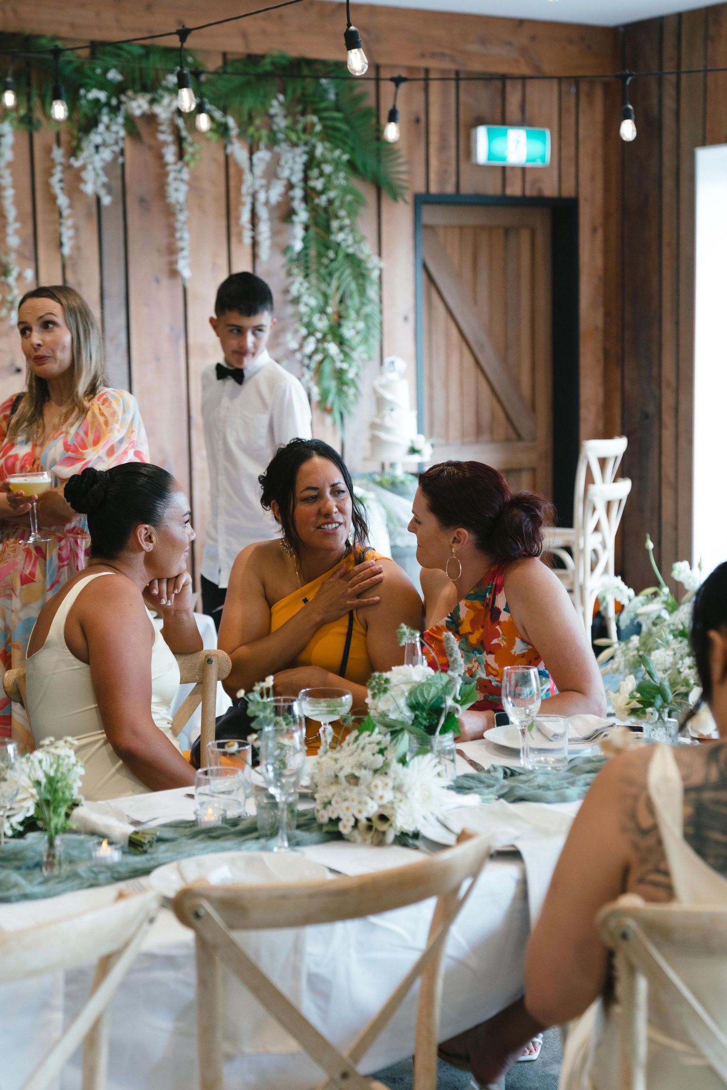 Wedding reception table setting in a rustic barn venue with string lights and floral decorations.