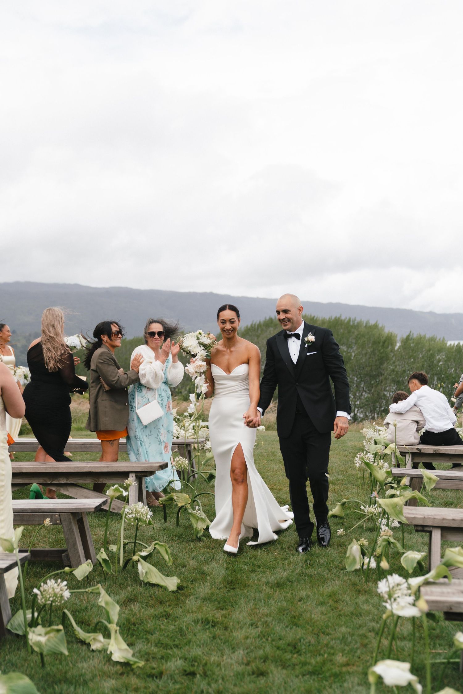 A wedding celebration on a hilltop venue with rustic wooden benches lining the aisle.