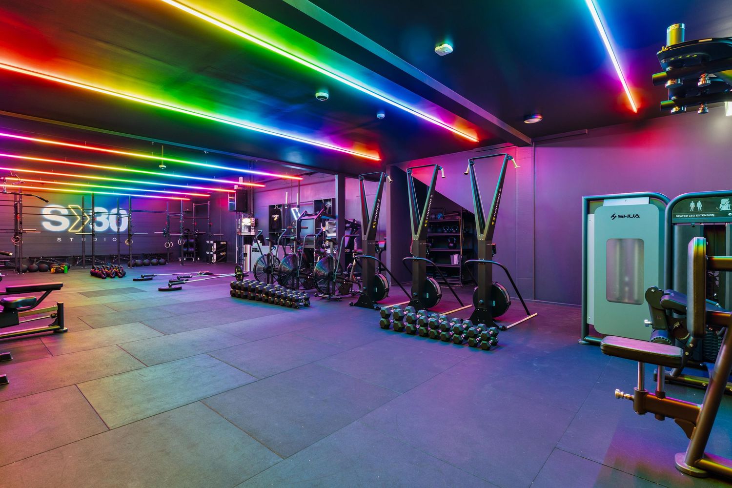 Modern gym space with weight training equipment under dramatic rainbow LED lighting and S30 branding.