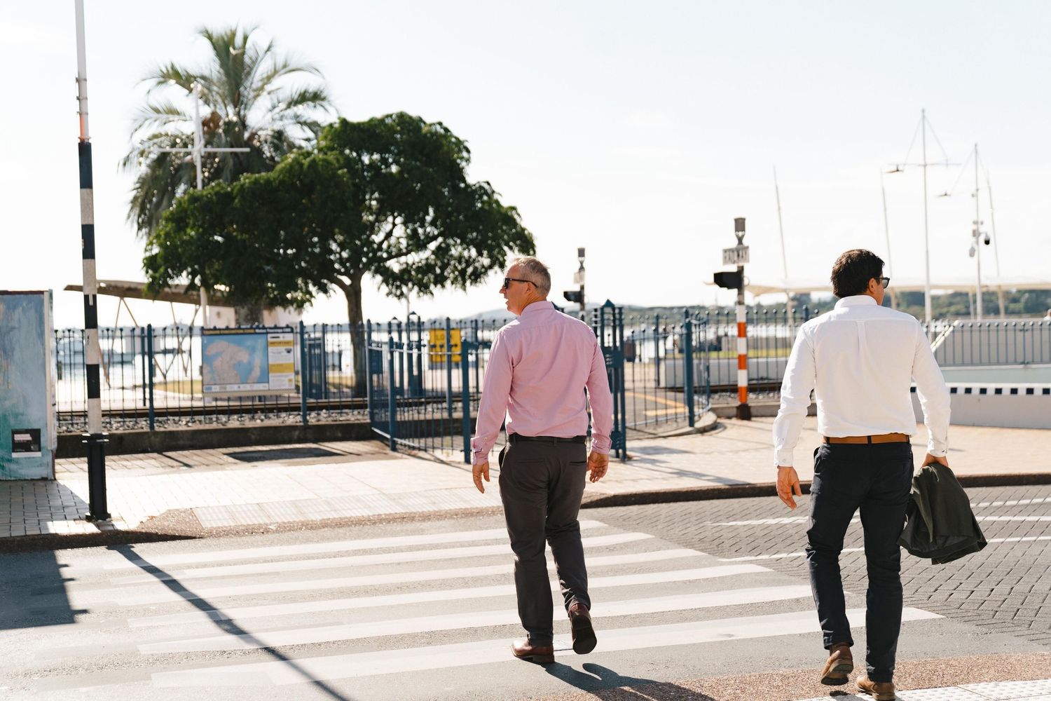 Two professionals walking through gated entrance area with palm trees in background.