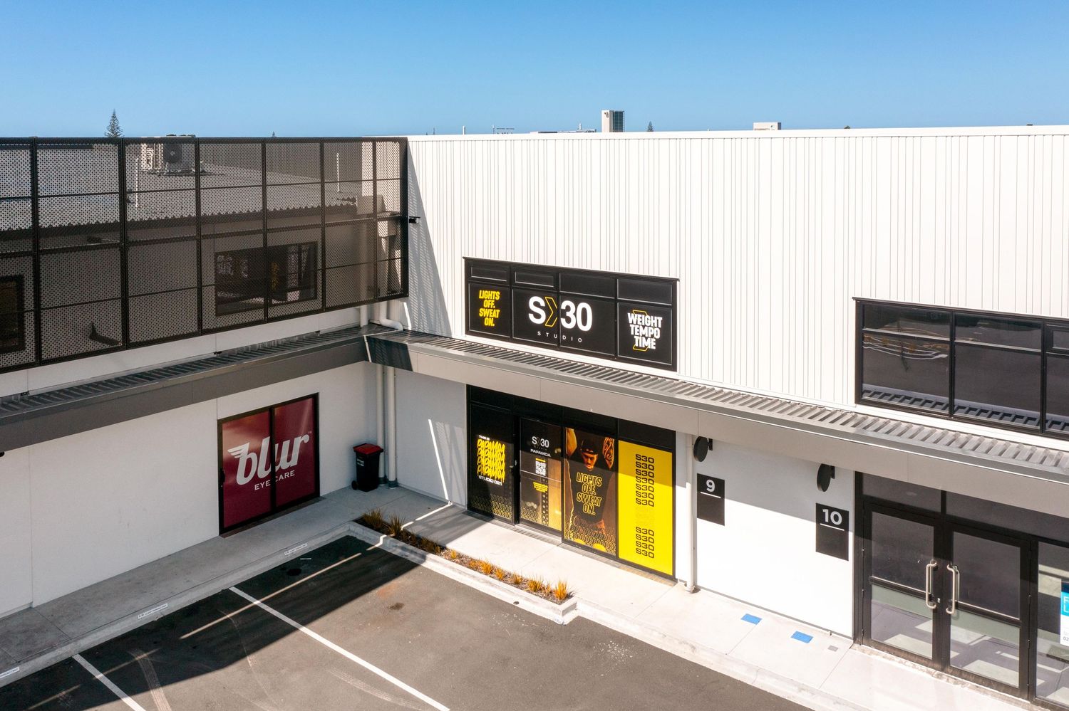 Modern retail storefront entrance with yellow door and parking spaces in front.