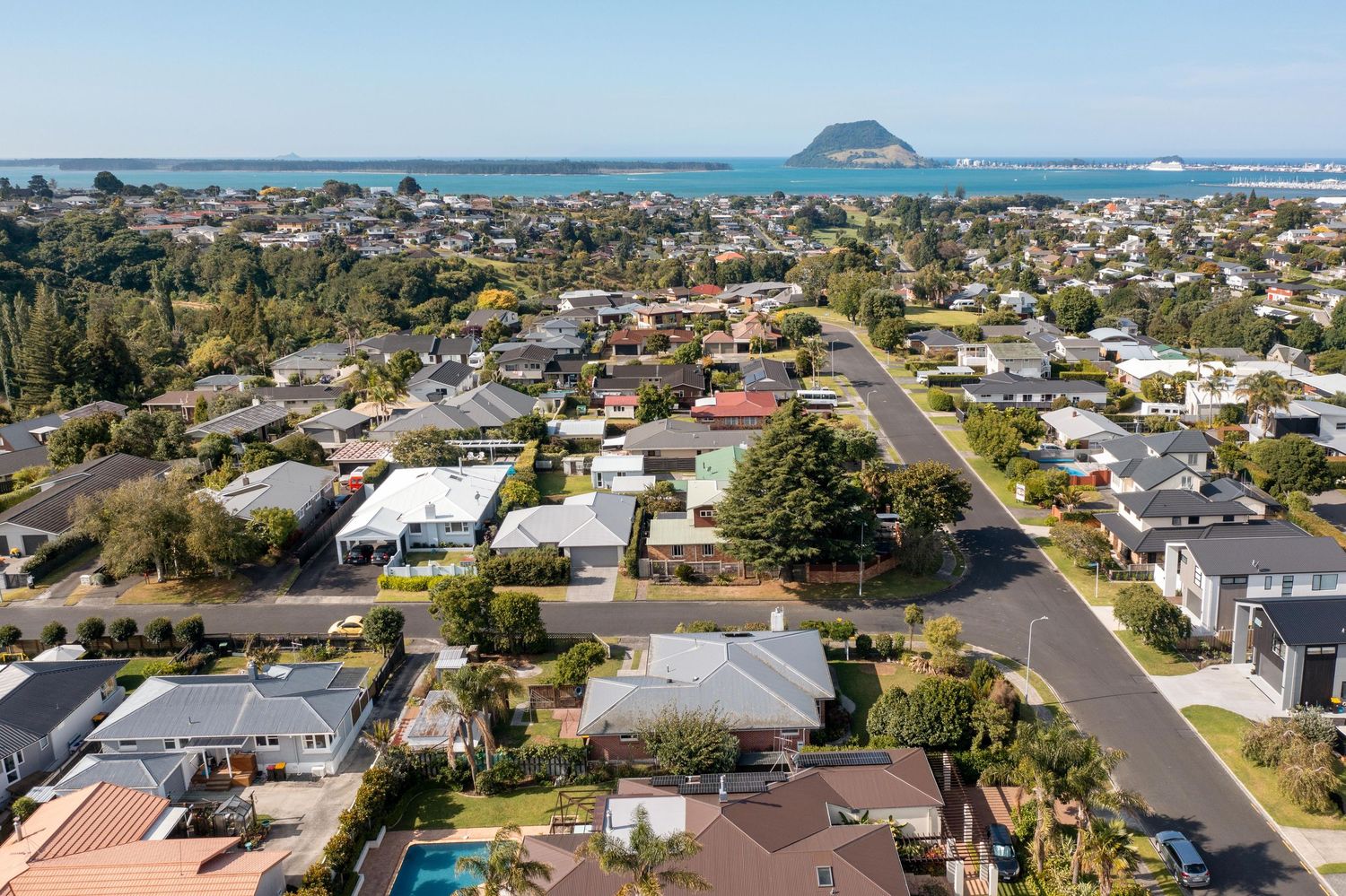 Aerial panoramic view of coastal residential neighborhood with houses facing Mount Maunganui in New Zealand.