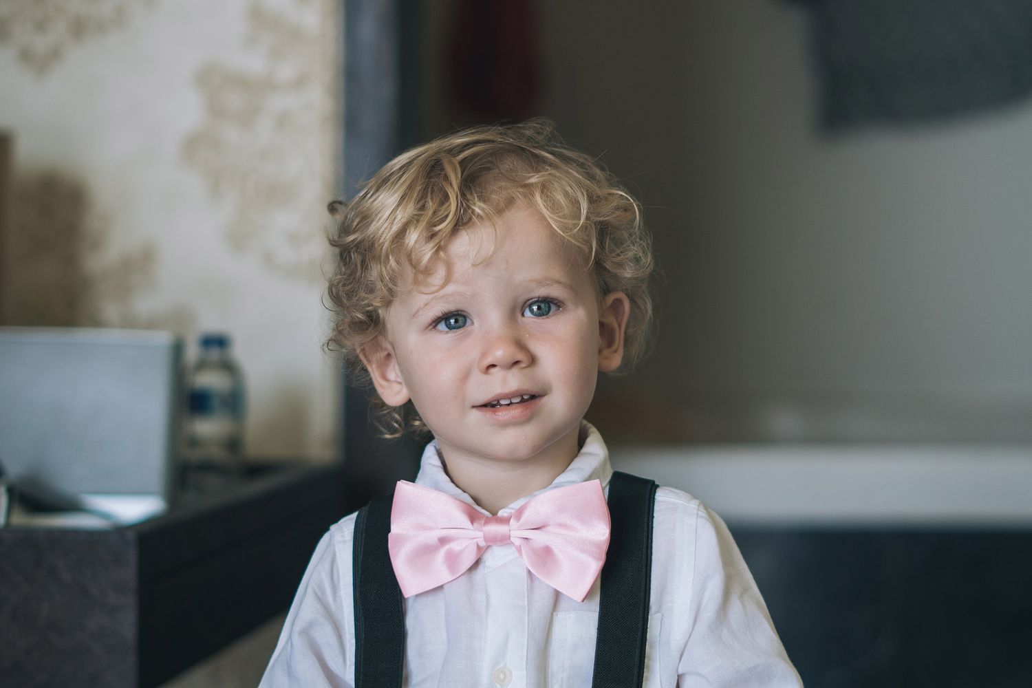 Young child in formal attire with a pink bow tie smiling.