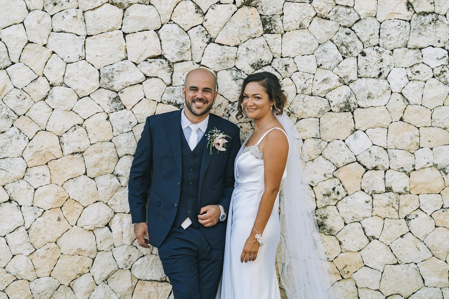 Newlywed couple posing against a textured stone wall during their destination wedding.