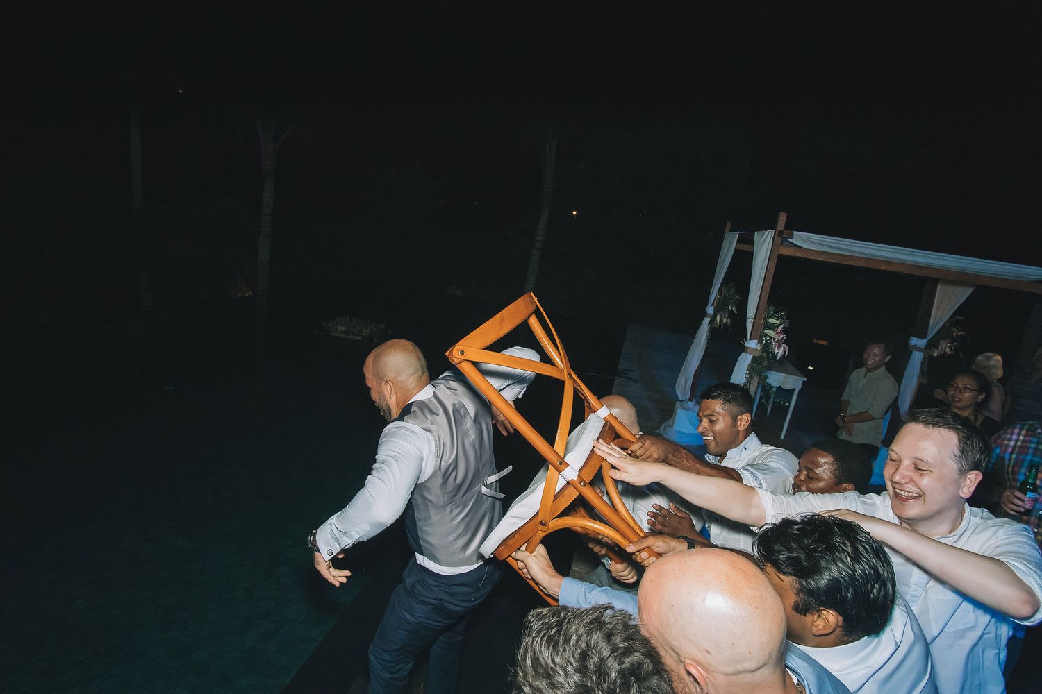 Energetic crowd of wedding guests dancing with raised arms at a nighttime reception.