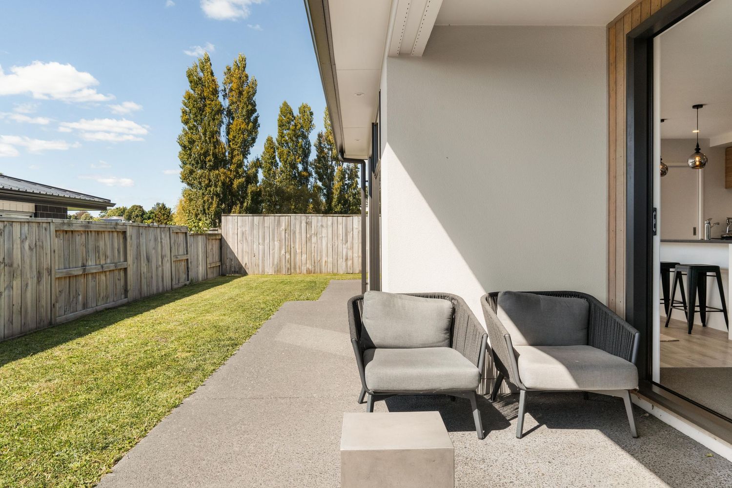 Modern outdoor patio area with grey lounge furniture and concrete flooring alongside a grassy backyard.