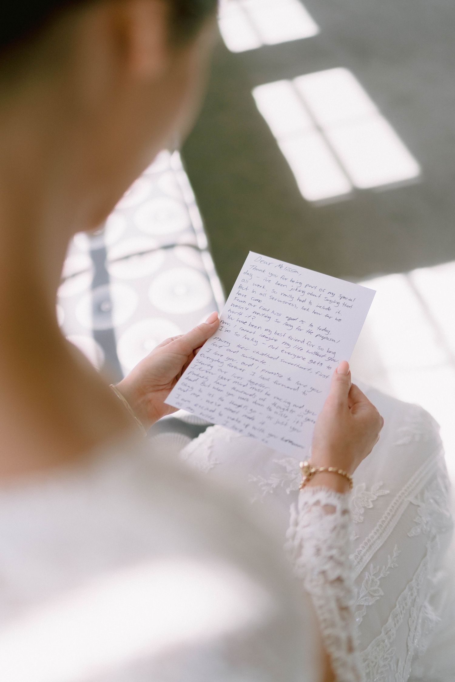 A handwritten letter or note being held and read in soft natural lighting with lace details visible.