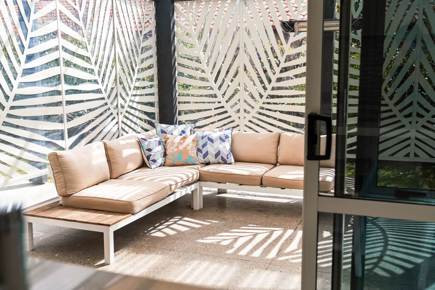 Outdoor lounge area with beige L-shaped sofa and decorative palm frond privacy screens.