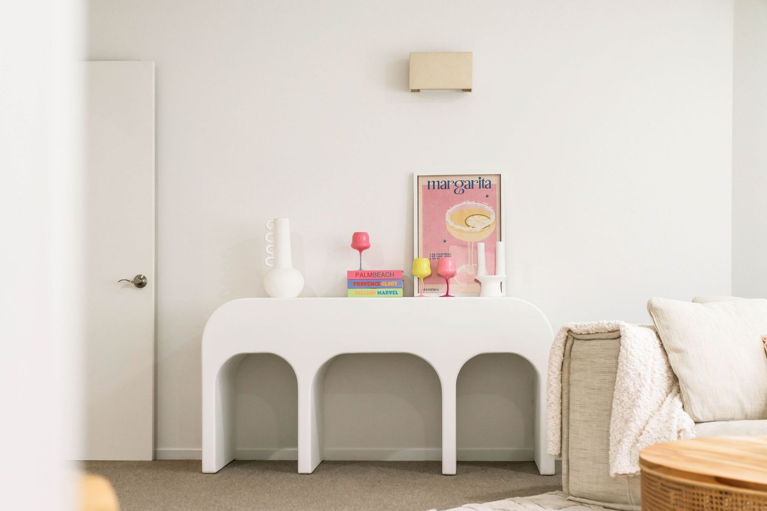 Modern white arched console table with decorative items and pink art print against a white wall in a minimalist room.