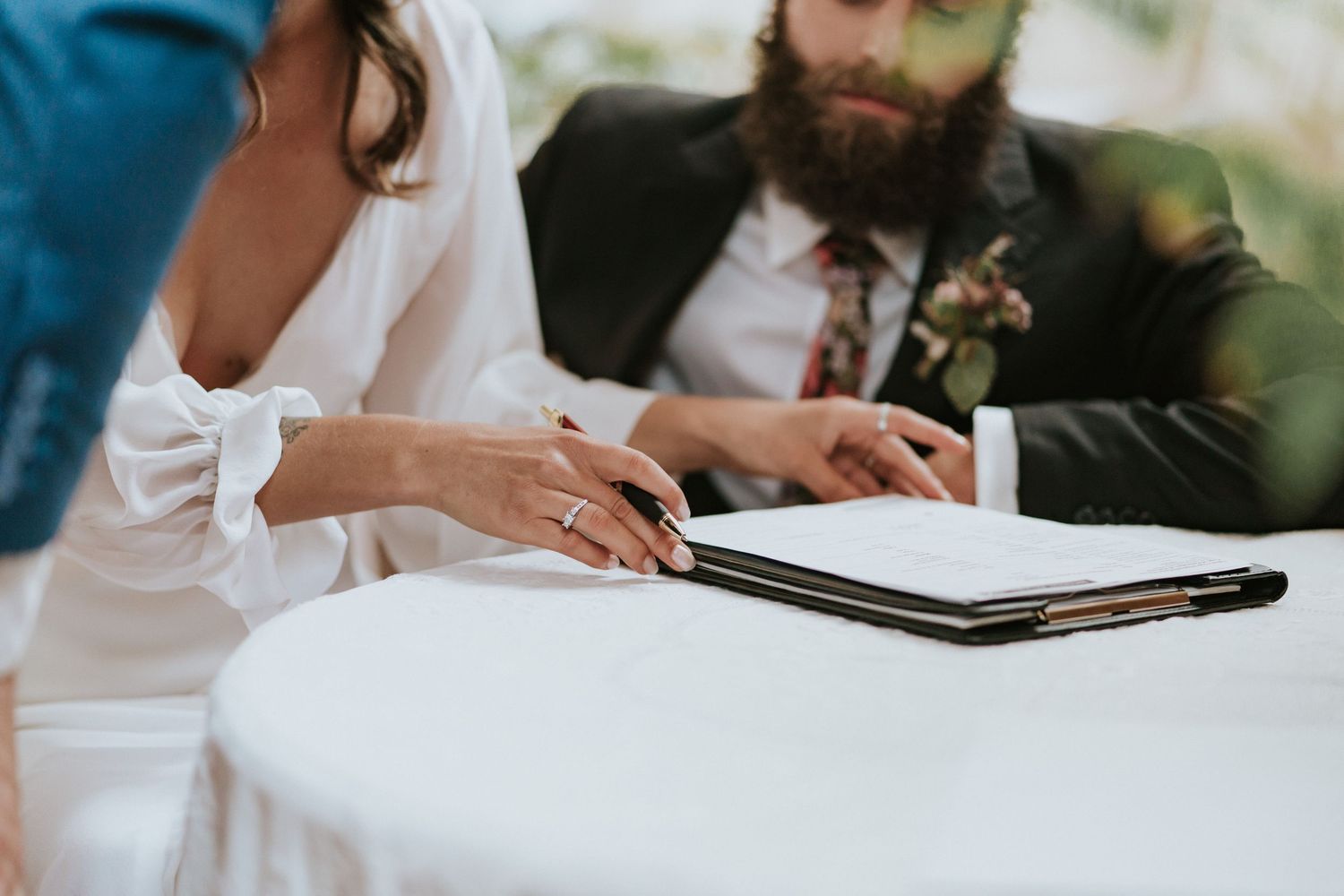 Hands holding a pen sign documents on a white table during a wedding ceremony.
