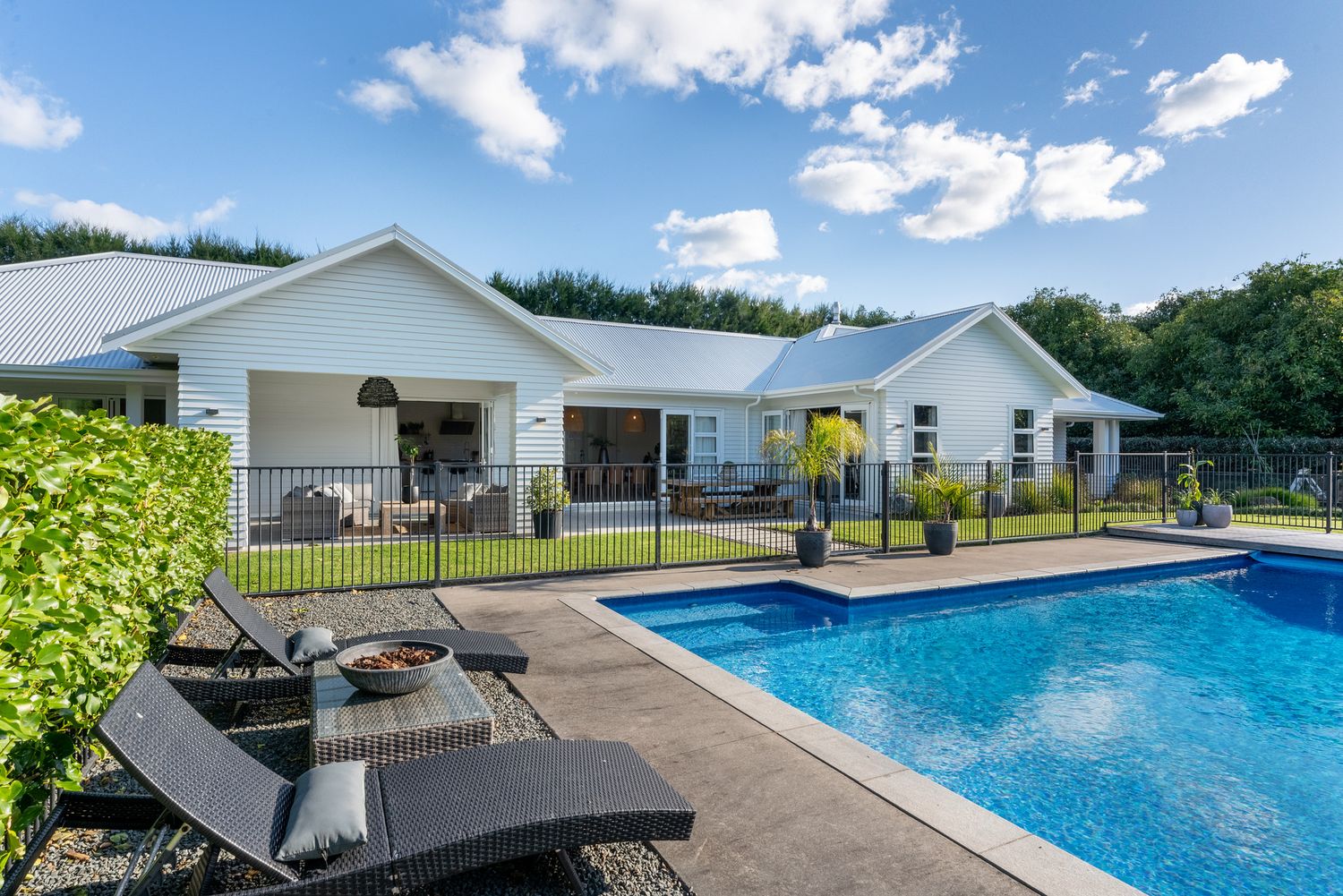 Modern white single-story home with in-ground pool and chaise lounge chairs on patio surrounded by landscaping.