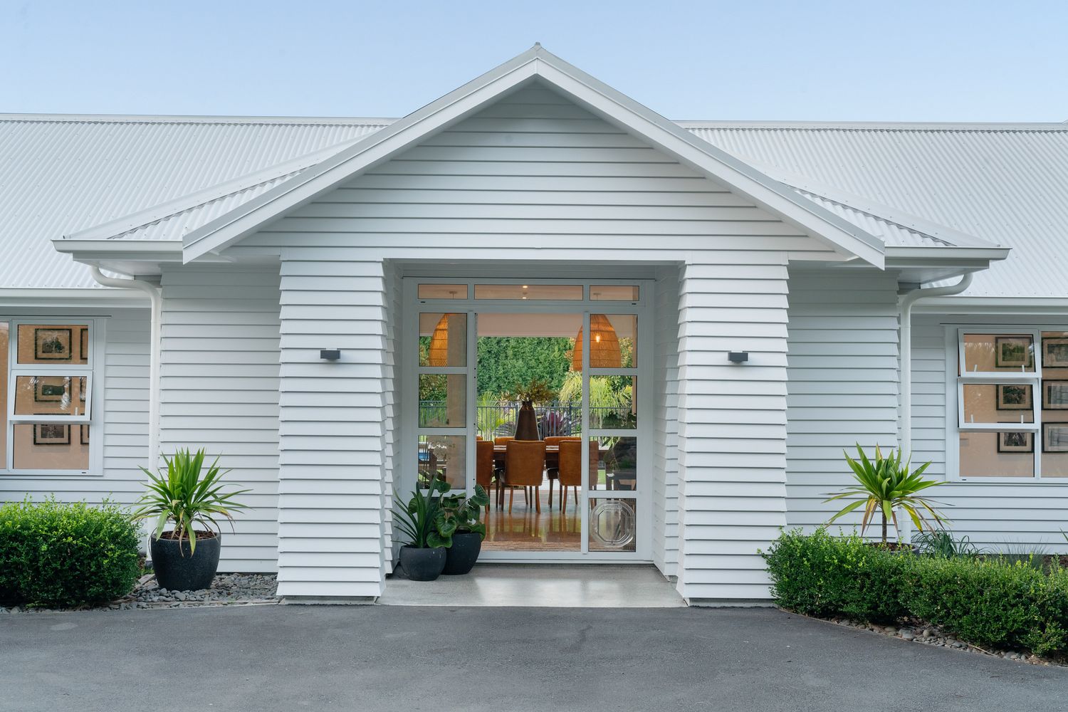White farmhouse-style entrance with symmetrical windows and potted plants framing a glass doorway.