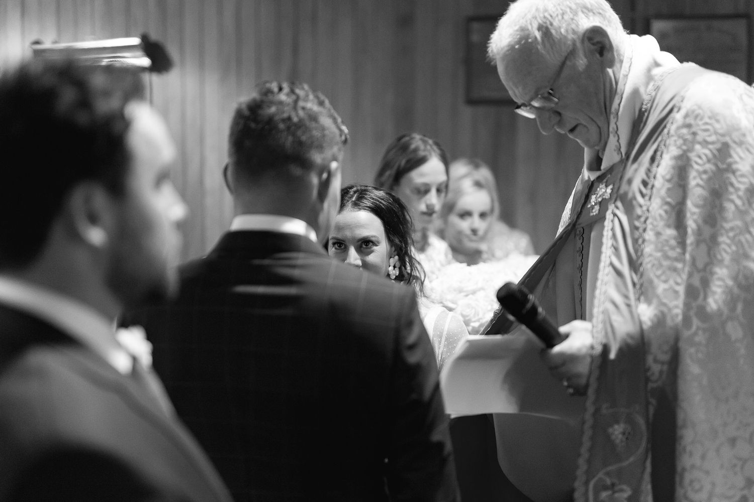 A black and white wedding ceremony moment showing a minister performing the service at the altar.