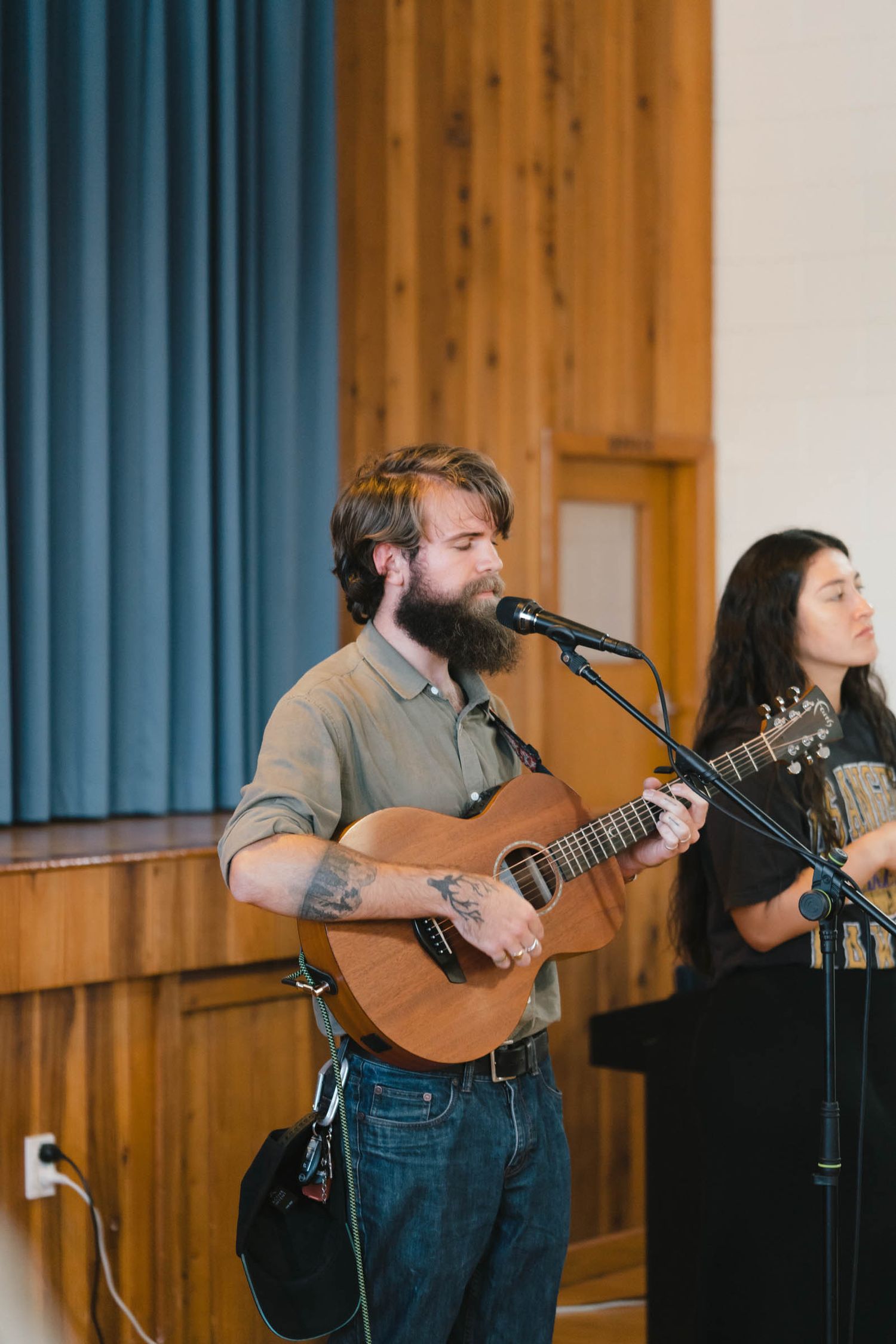 Musicians performing with acoustic guitar and microphones on a wooden stage.