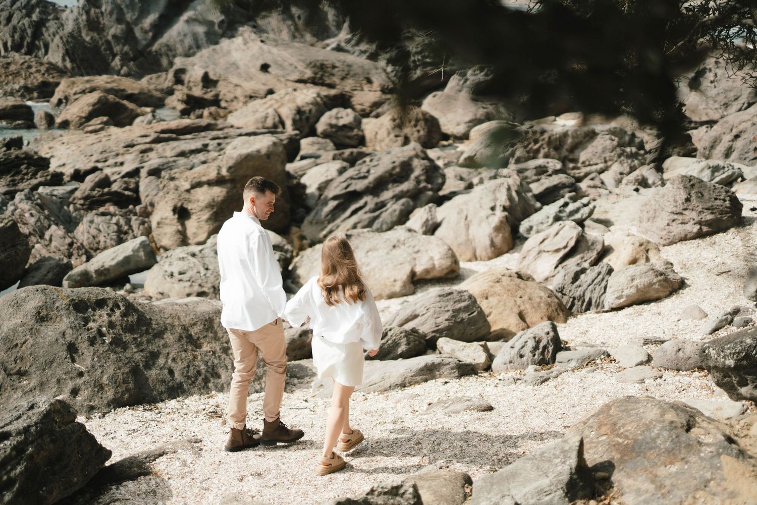 Active young climber wearing light-colored clothing scales rocky terrain while bouldering outdoors in scenic location.