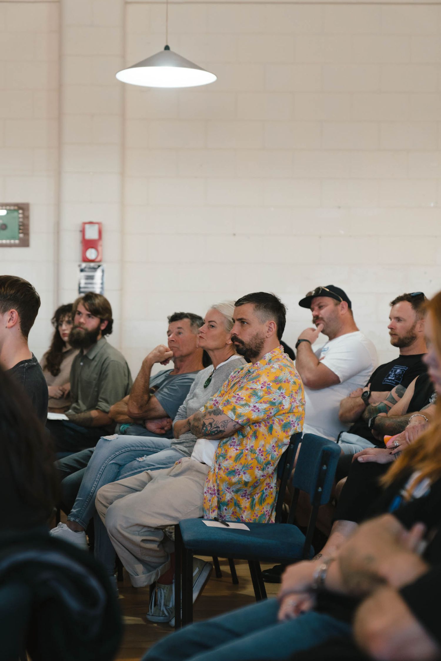 An attentive audience sits in chairs watching a presentation in an indoor venue.