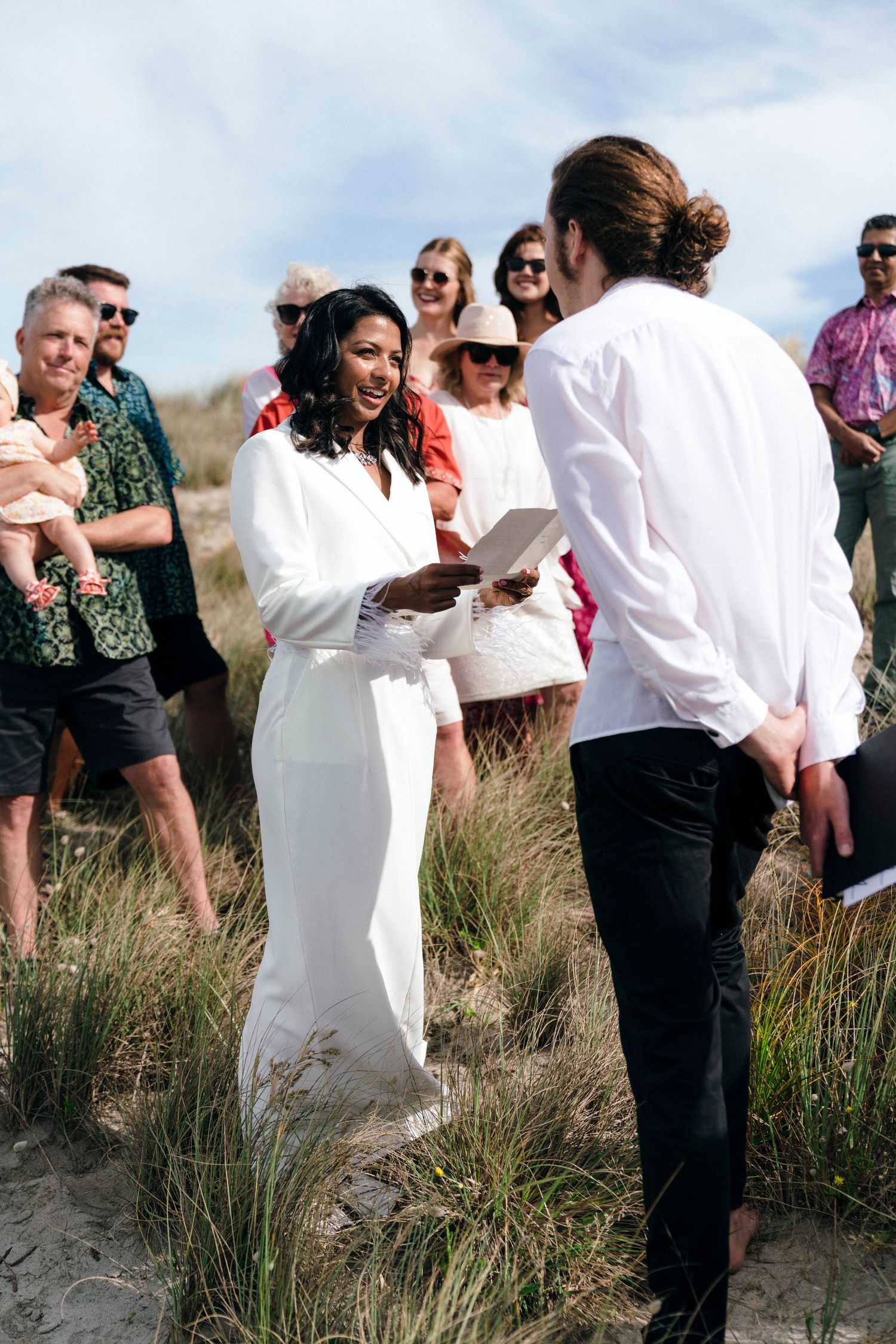 Wedding party in white and black attire gathering on scenic coastal sand dunes.