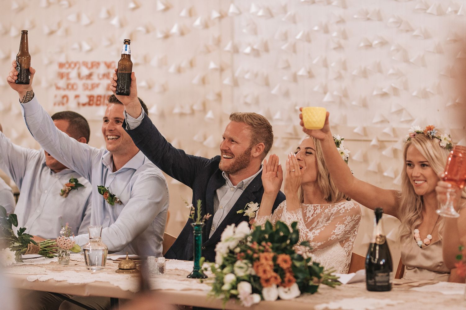Wedding party raising drinks in celebration during reception dinner with floral centerpieces and champagne bottles.