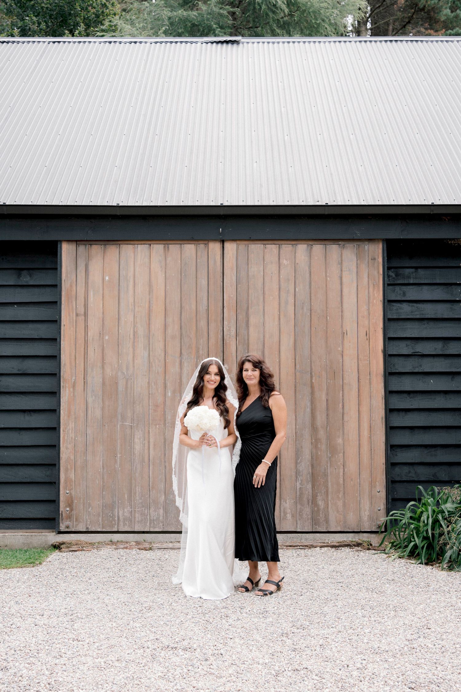 Black barn building with natural wood doors and metal roof creates rustic wedding backdrop.