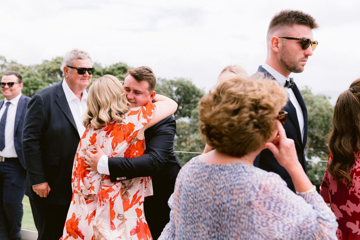 Wedding guests mingling and embracing at an outdoor celebration.