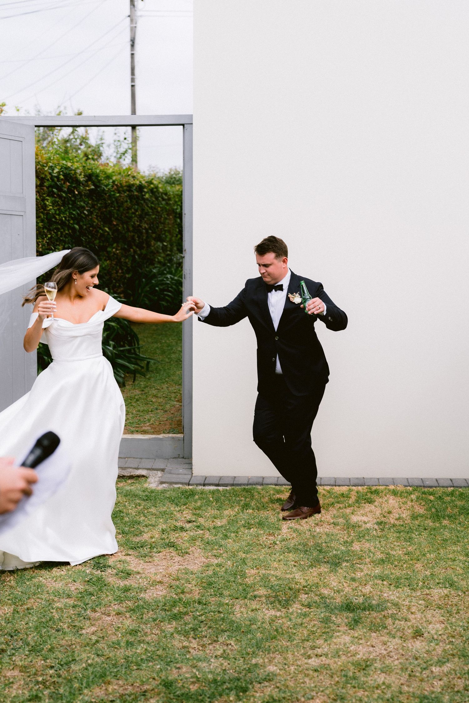 Playful wedding couple dancing and twirling in front of a white building.