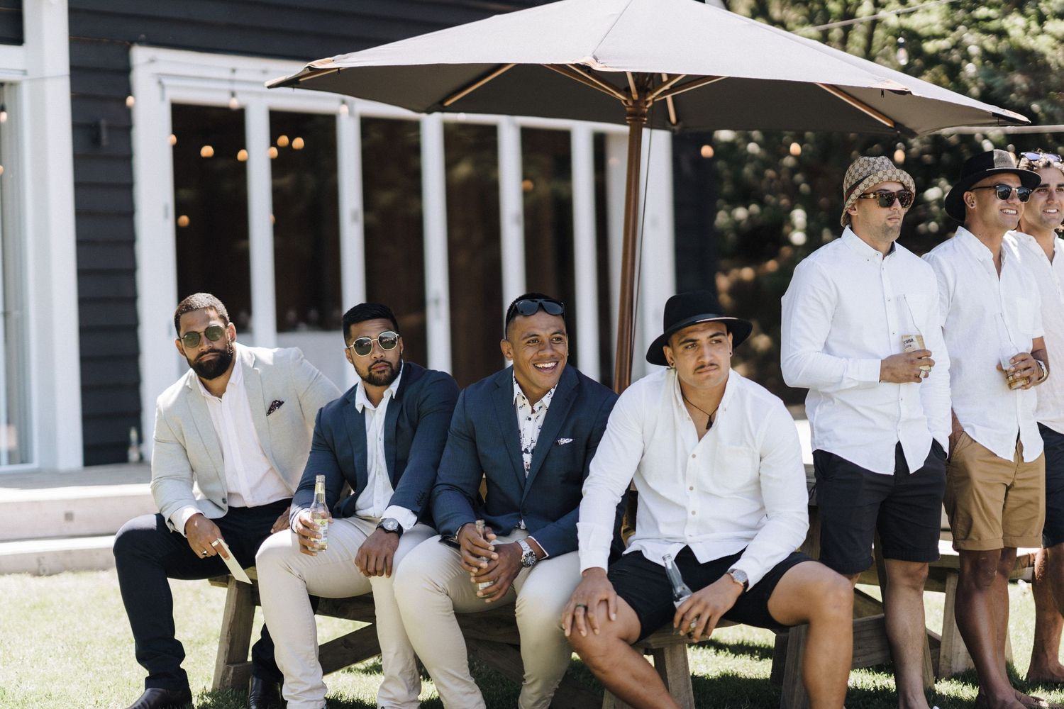 Wedding party relaxing outdoors in casual summer attire under white tents.