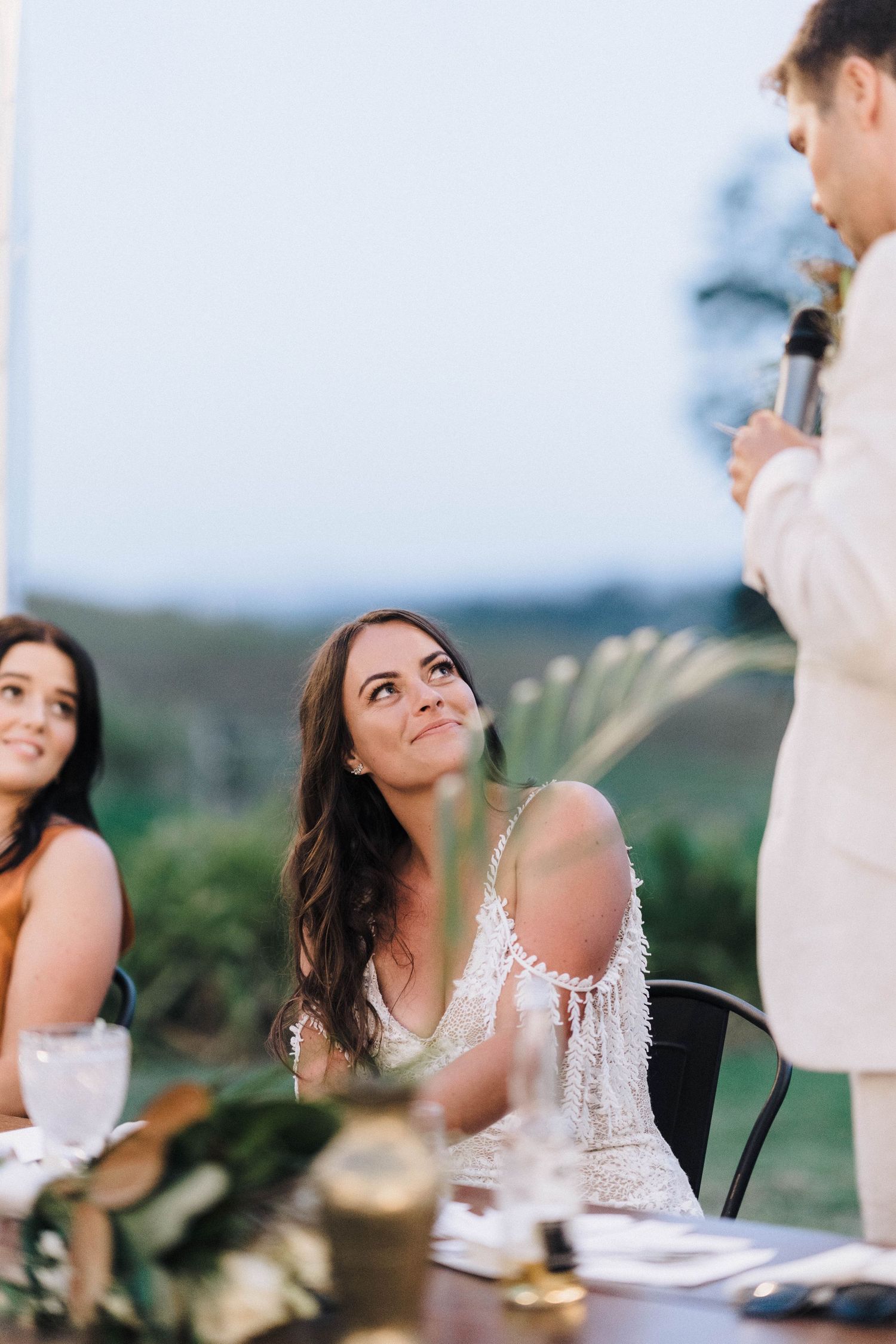 A beautiful candlelit outdoor wedding reception dinner scene with guests seated at a rustic table at dusk.