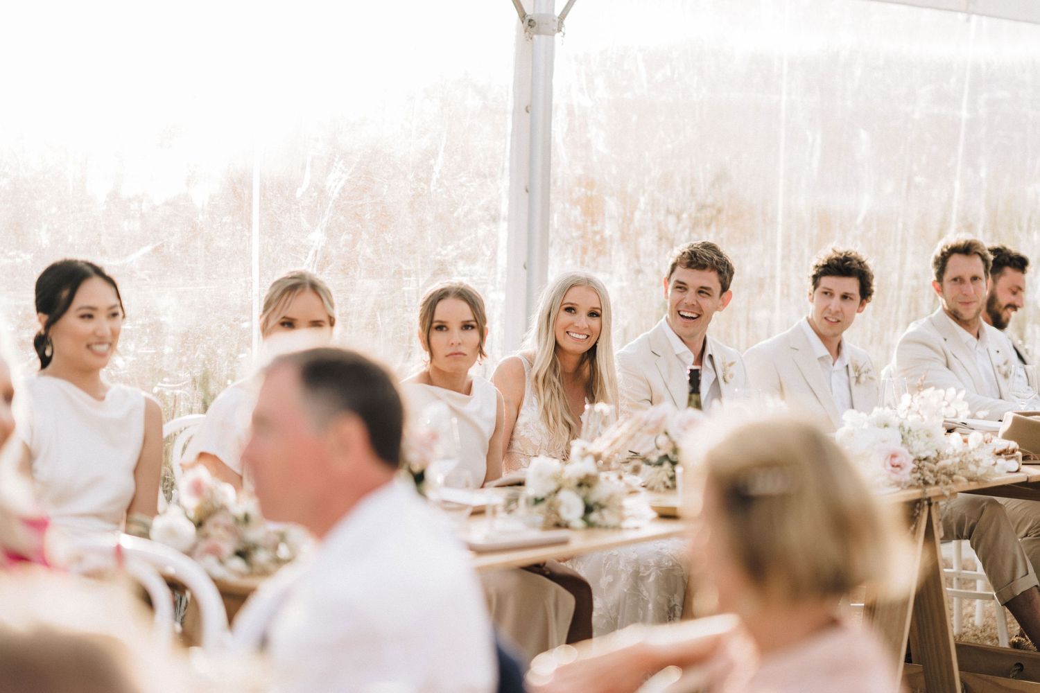 Elegant white reception tent interior with tables and chairs set up for a beach wedding celebration.