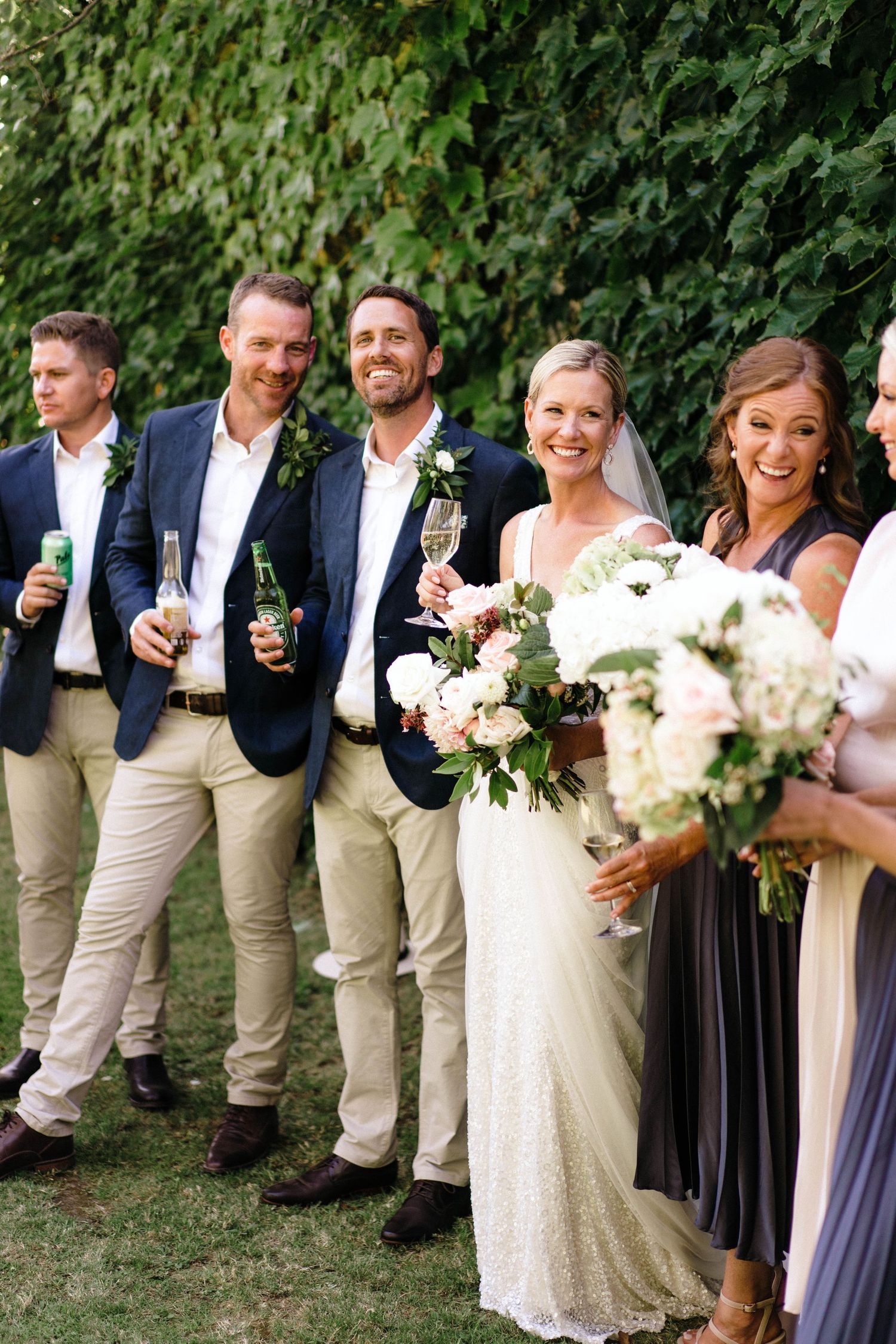 Wedding party poses together on grass with bridesmaids in navy dresses and groomsmen in light suits.
