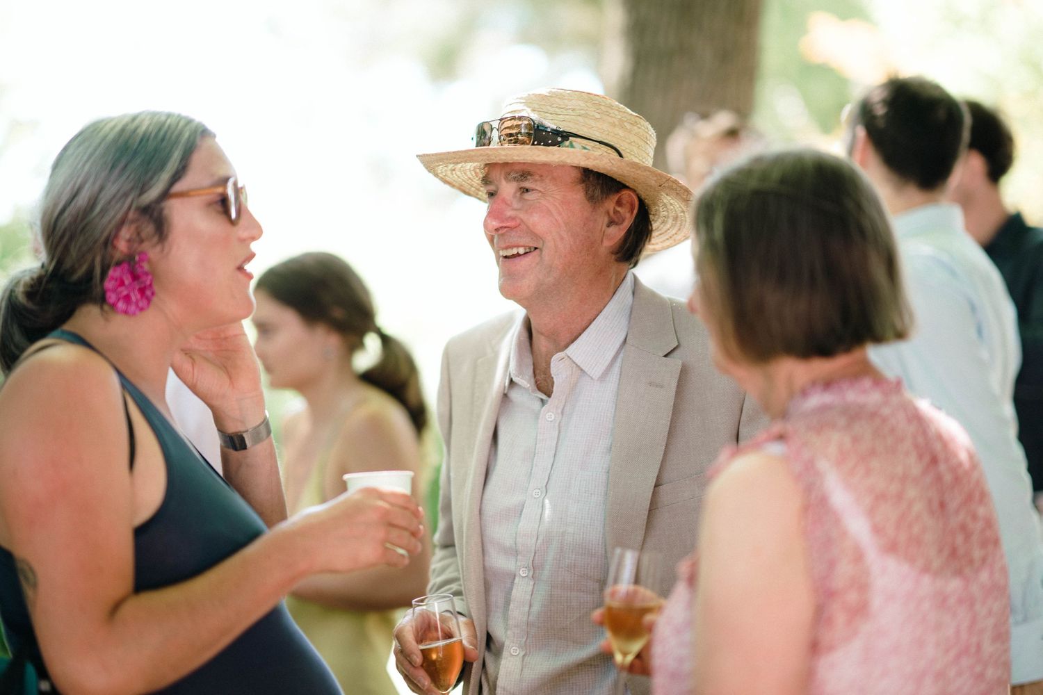 Wedding guests socializing and enjoying drinks at outdoor summer celebration.