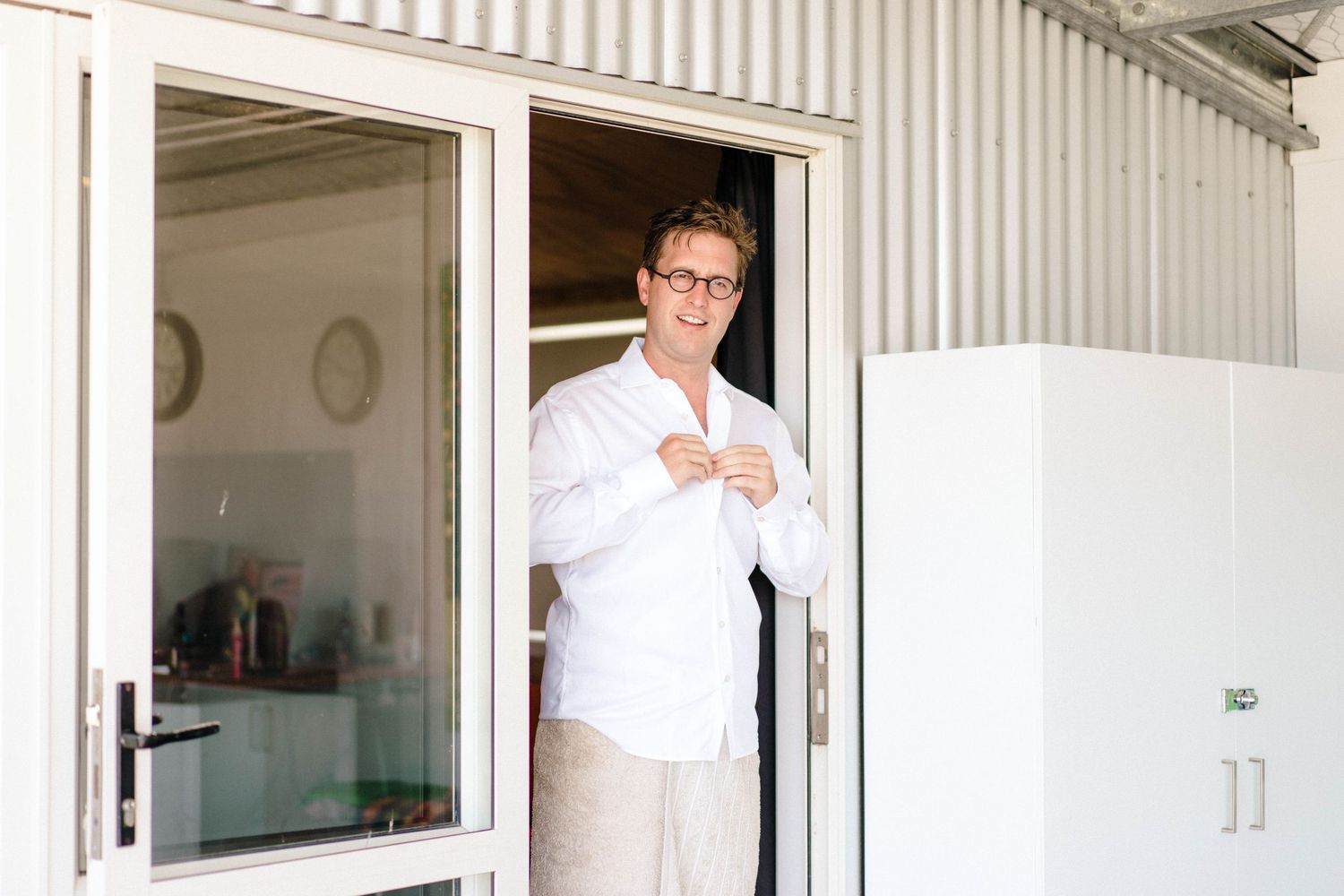 Person standing in doorway of white building holding something in their hands.