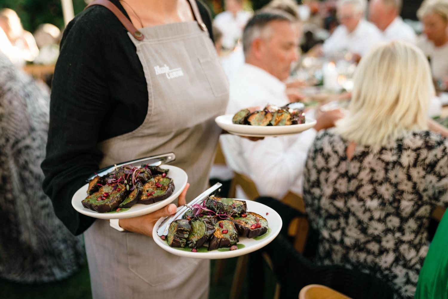 Wedding guests serving themselves food from buffet-style plates at an outdoor reception.