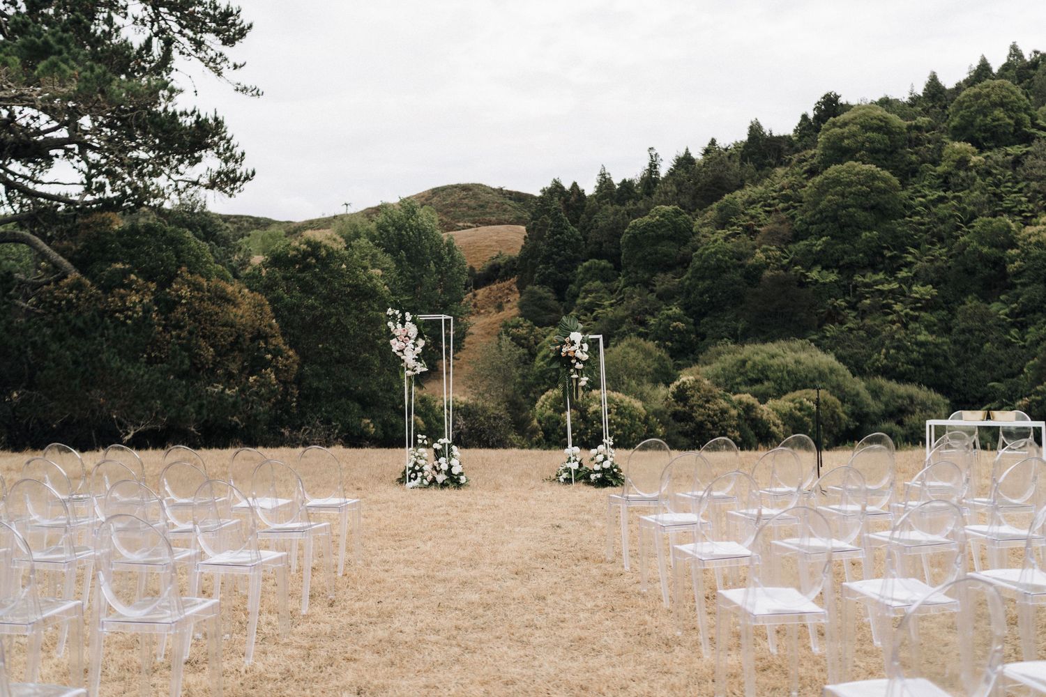 White chairs set up for an outdoor wedding ceremony against a backdrop of rolling hills and forest.