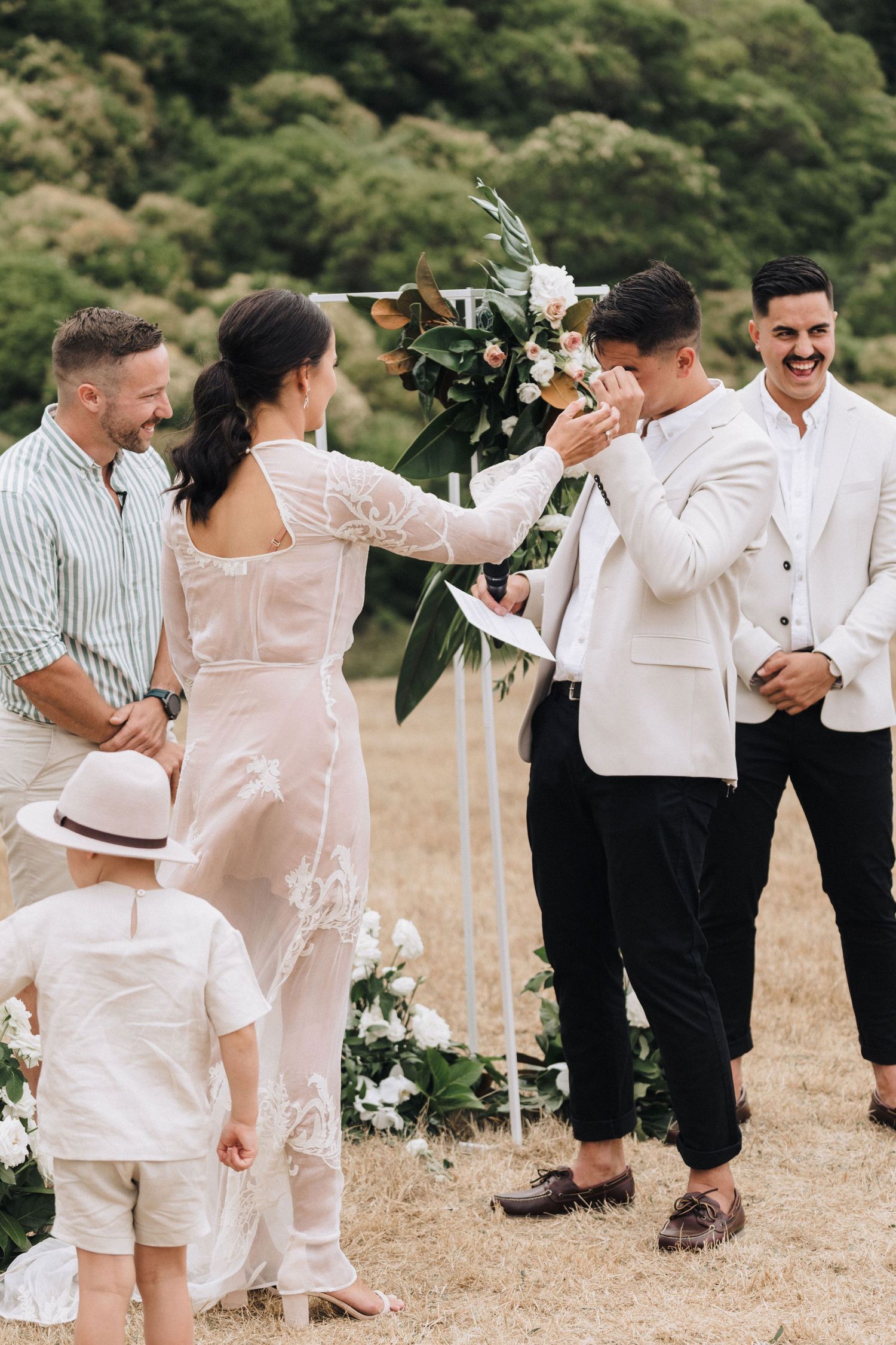Wedding party members sharing an emotional moment during outdoor ceremony with floral decorations.