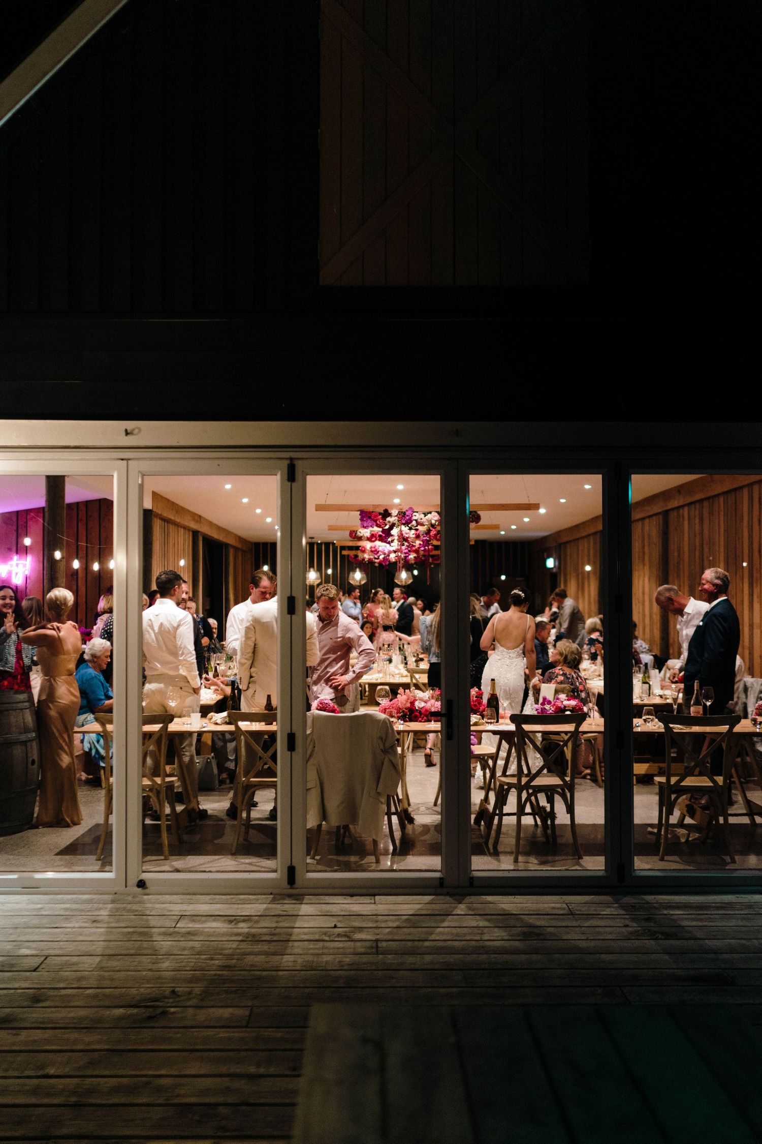 Evening view of a lit reception venue through glass windows with guests dining inside.
