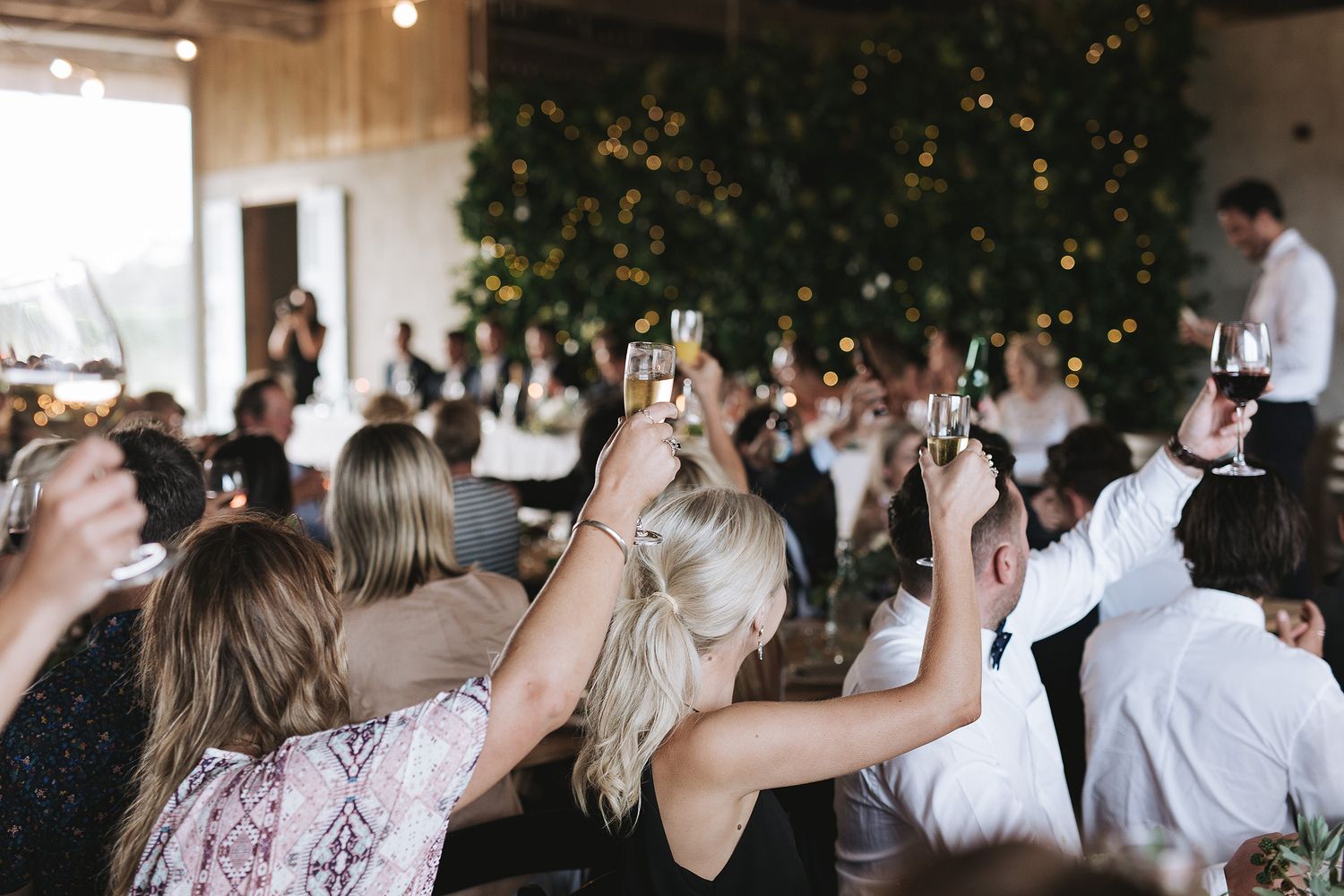 Wedding guests raise their phones and cameras to capture a moment during an indoor reception ceremony.