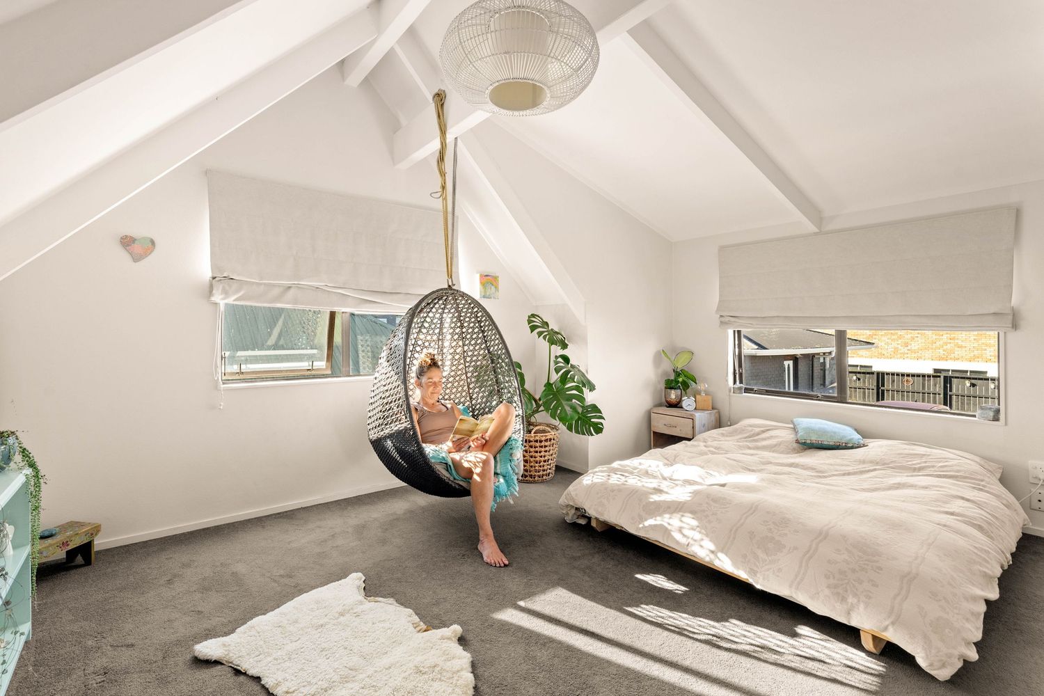 Modern bedroom with vaulted ceiling features a hanging egg chair, white bedding, and gray carpeted floors.