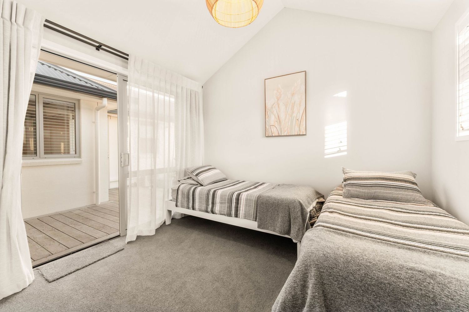 Contemporary bedroom with gray bedding, white walls, and sheer curtains offering a serene and bright ambiance.