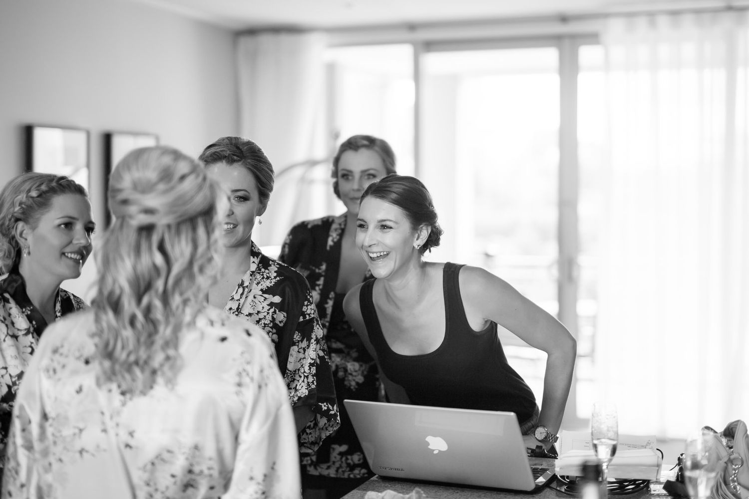 A group gathers around a laptop in a bright room, sharing a lighthearted moment while collaborating together.