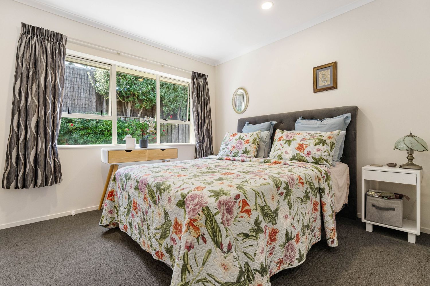 Cozy bedroom featuring floral bedding, striped curtains, and white walls with natural light from a large window.