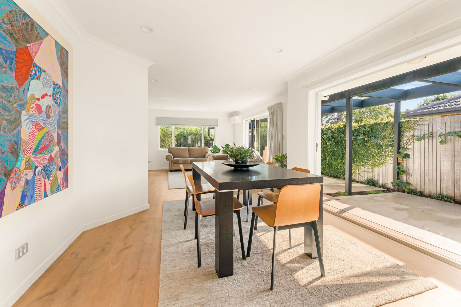 Bright dining area with modern furniture and colorful wall art adjacent to glass sliding doors.