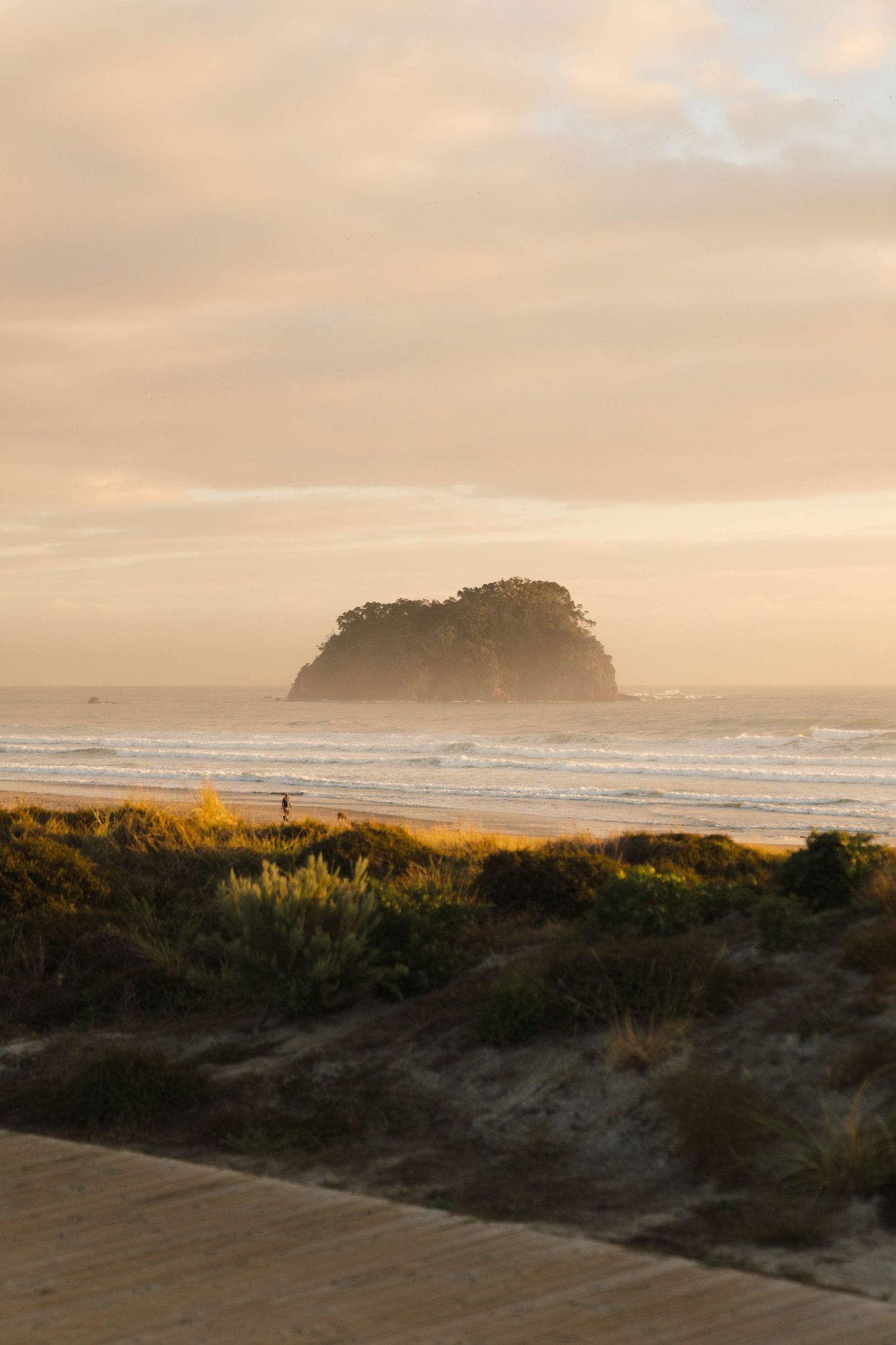 Misty coastal sunrise over a dramatic rocky island formation on the beach.