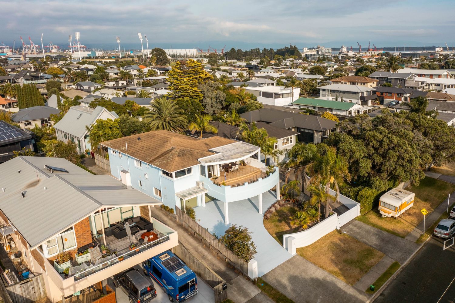Aerial view of coastal neighborhood showing residential houses, blue skies, and city skyline in the distance.