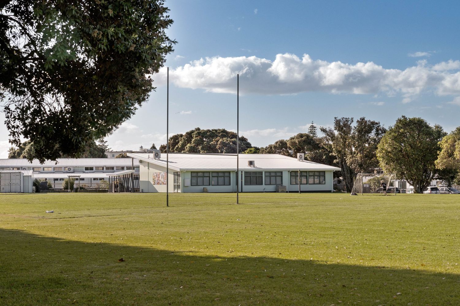 Expansive green sports field with buildings visible in the background under blue sky.