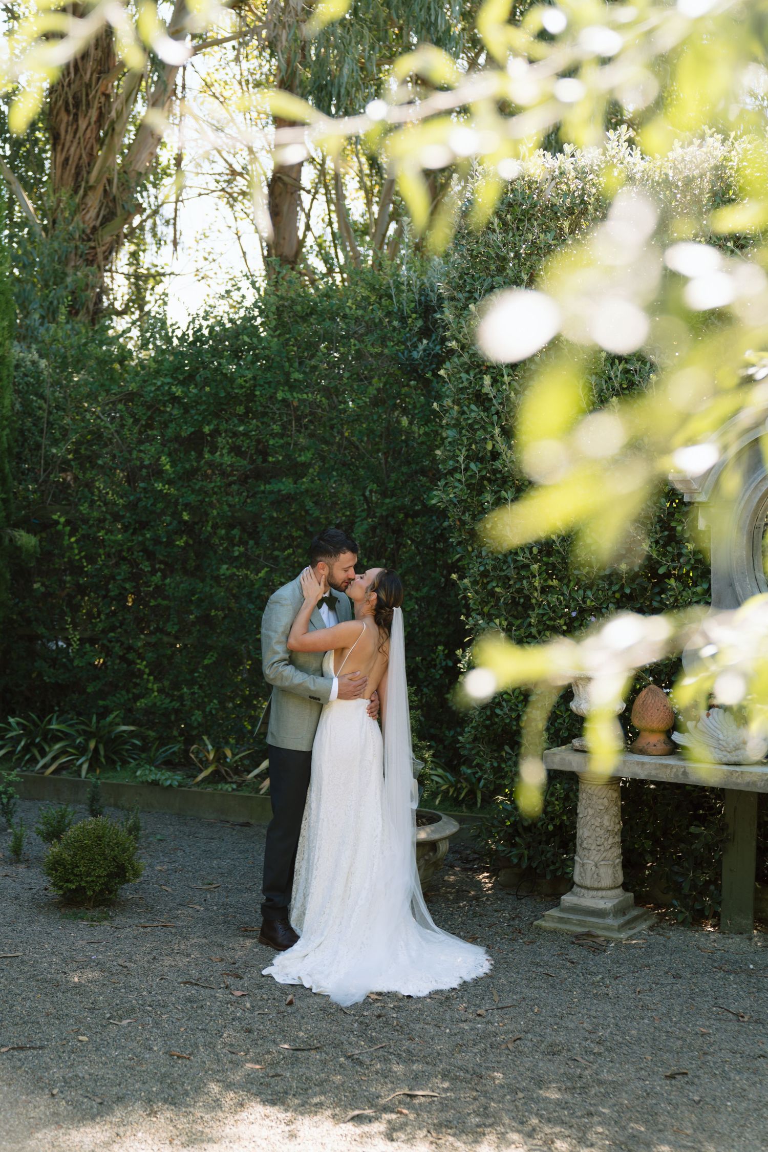 Bride and groom share a romantic kiss in a lush garden setting, bride wearing elegant white gown with veil. Photographer Bryony at Newfound.