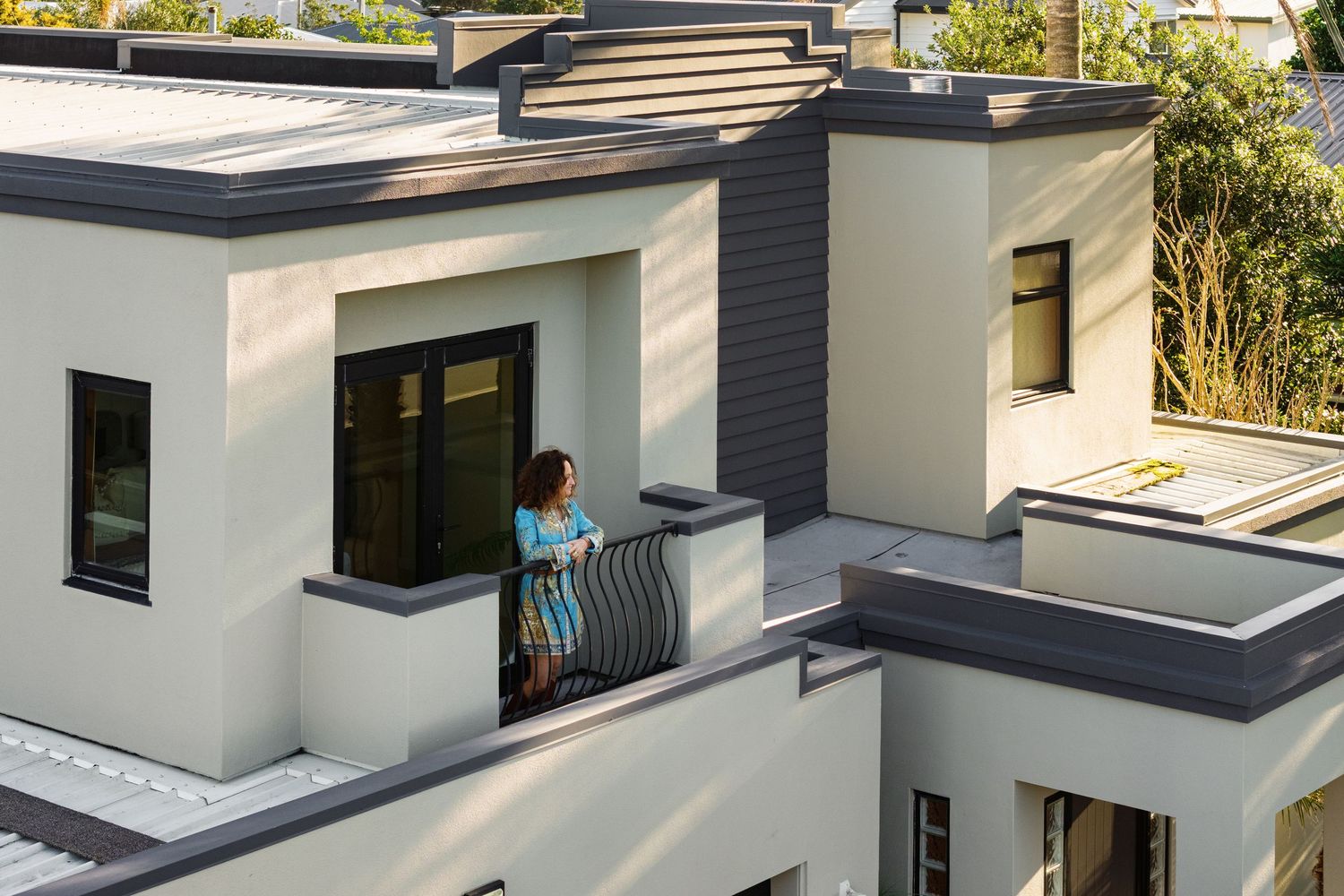 Woman standing on a modern white balcony with dark railings on a multi-level contemporary home exterior.