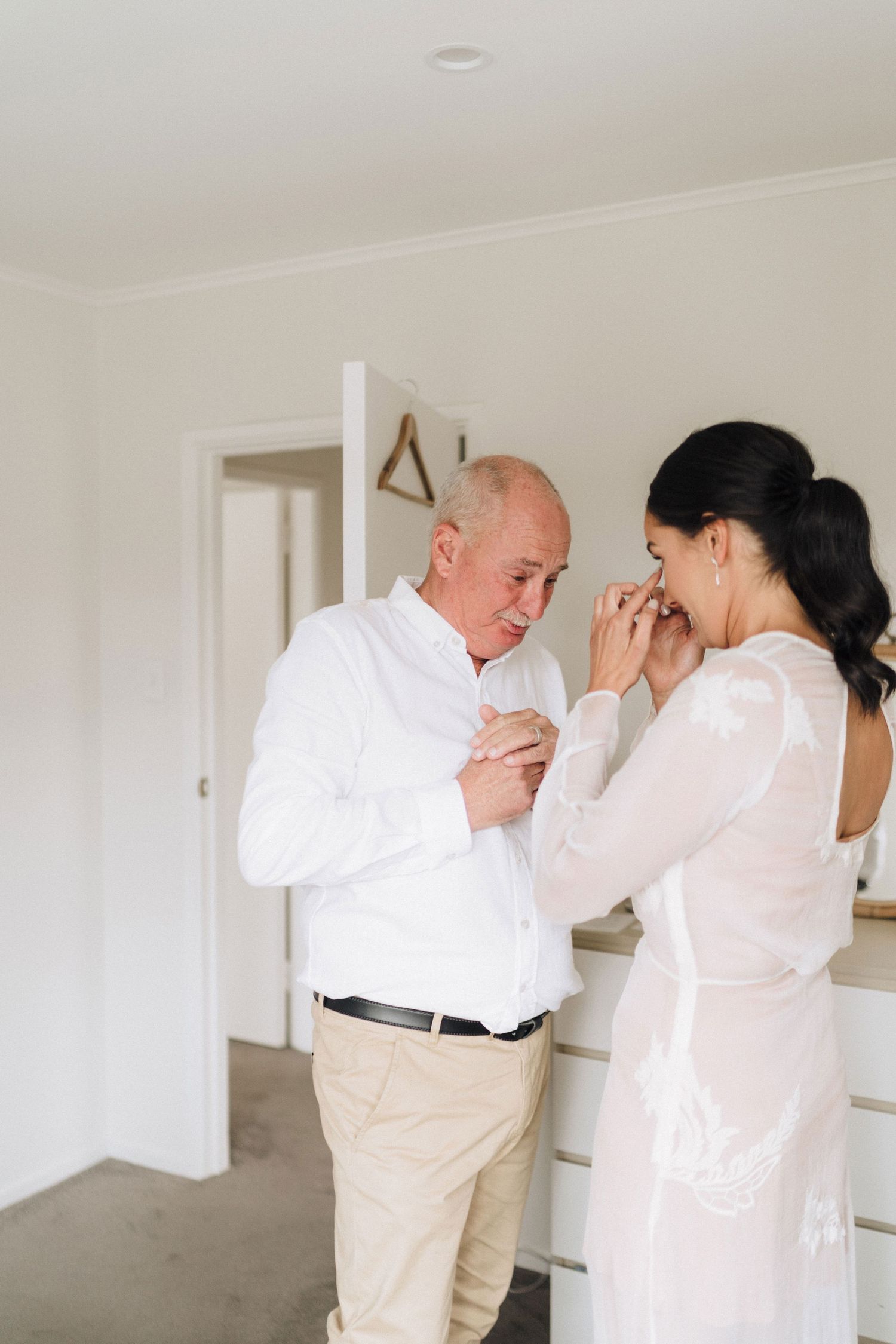 Emotional moment shared between two people in white attire during wedding preparations.