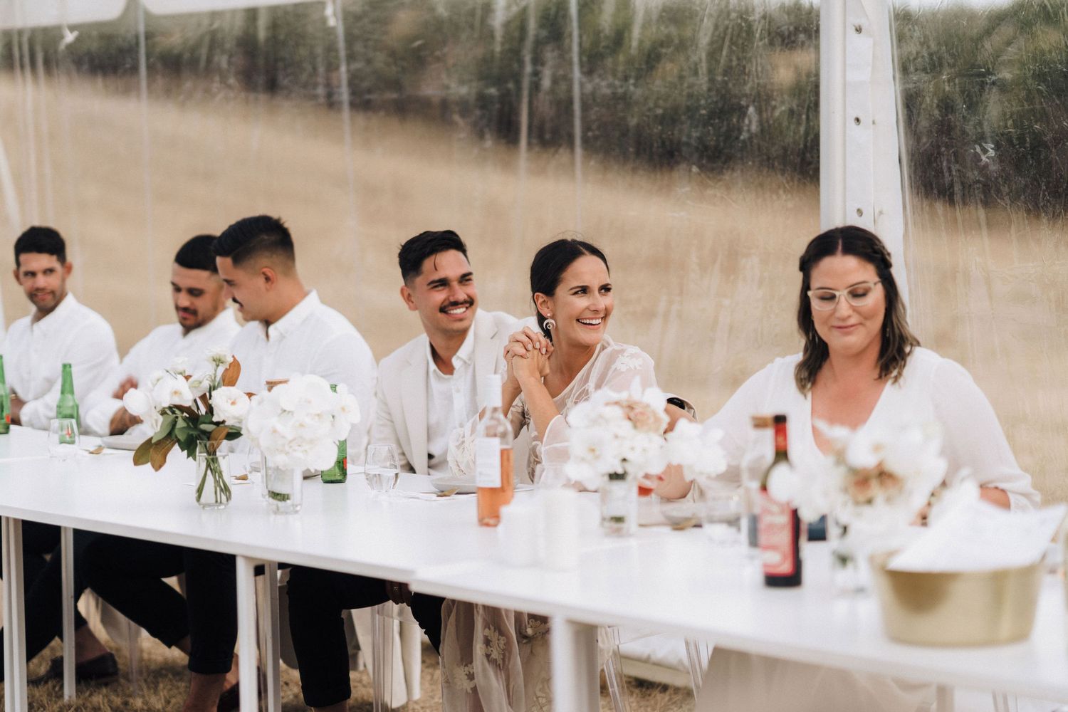 Long white dining tables set up for an outdoor celebration with natural scenery.