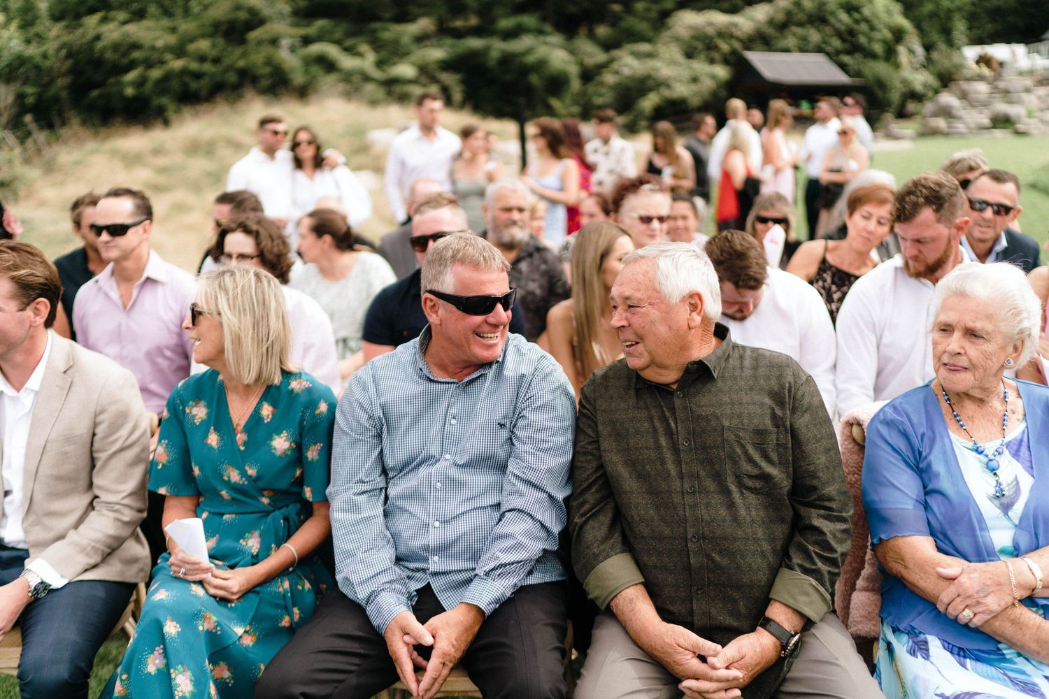 Wedding guests seated in rows watching outdoor ceremony surrounded by greenery.