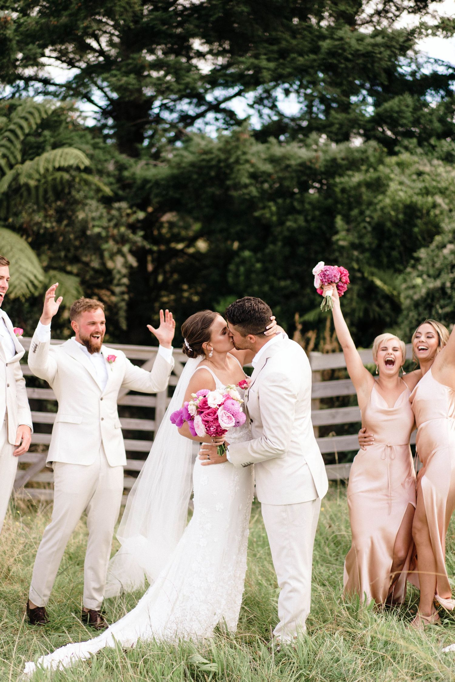 Wedding party celebrating outdoors with bright pink flowers and light-colored attire.